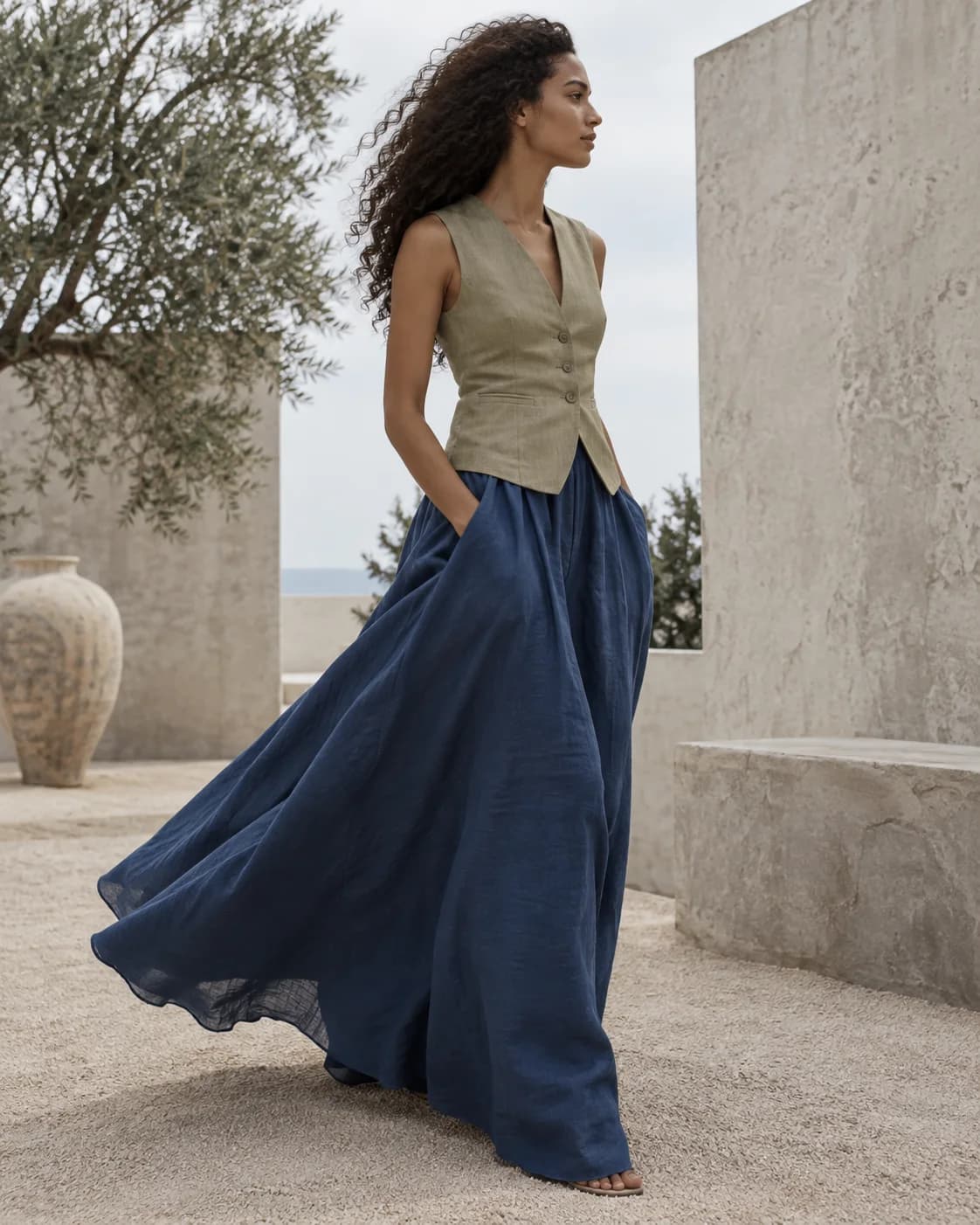 a woman in profile; a cobalt pleated skirt and white knit; a sunlit concrete courtyard